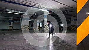 Skateboarding training. A young man skateboarding inside the parking lot, stops, takes the board in hand and goes