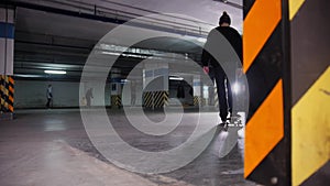 Skateboarding training. A young man skateboarding inside the parking lot, stops, takes the board in hand and goes