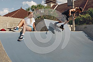 Skater Friends In Skatepark. Girl Sitting On Concrete Ramp, Guy Riding On Skateboard