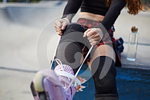 Skater girl putting on aggressive in-line skates in a skatepark. Female athlete tying laces and preparing for a ride