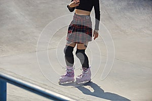 Skater girl riding on aggressive in-line skates in a concrete skatepark. Unrecognizable young female person skating outdoor in a