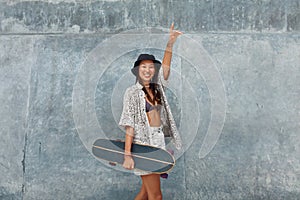 Skater Girl With Skateboard Portrait. Asian Teenager In Casual Outfit Posing Against Concrete Wall At Skatepark.