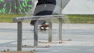 Skater make grind feeble 180 on rail in skatepark, close-up view in slowmotion