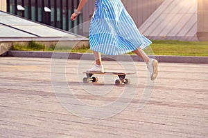 Skater woman in dress is training on longboard, doing a trick outdoor in a public park. Close up on leg kick off.