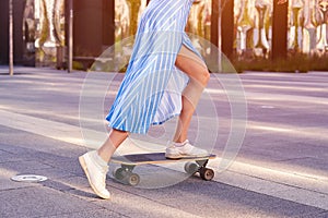 Skater woman in dress is training on longboard, doing a trick outdoor in a public park. Close up view on shoes.