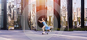 Skater woman in dress is training on longboard, doing a trick outdoor in a public parkÑŽ