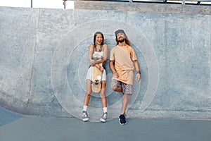 Skaters. Girl And Guy At Skatepark. Portrait Of Hipster Couple In Casual Outfit With Skateboard Against Concrete Wall