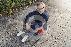 Skating - sport for everyone. Caucasian gray-haired man dressed in business casual way sitting on neon orange skateboard