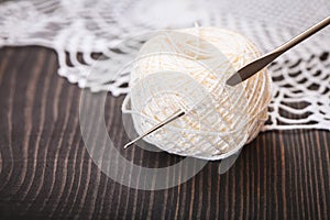 Skein of white yarn and crochet hook on a wooden table