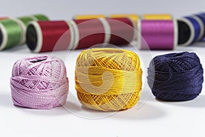 Skeins of cotton thread in foreground with bobbins for sewing machines in the background