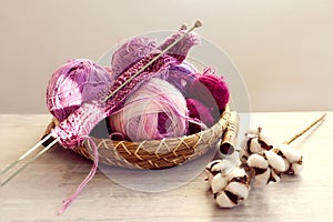 Skeins of multicolored yarn in purple tones, knitting needles on a decorative tray, a branch of cotton on a light table, gray