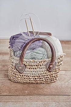 Skeins of yarn, wooden circular knitting needles in handmade straw basket on wooden table