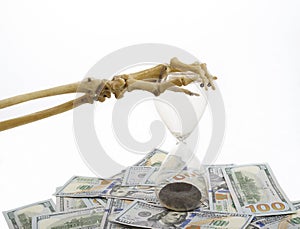 Skeleton fingers holding sand-glass placed on dollars. concept of time - money and death.