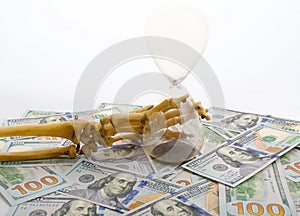 Skeleton fingers holding sand-glass placed on dollars. concept of time - money and death.