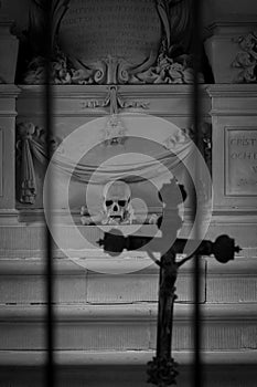 Skeleton head and bones beyond bars with a religious cross as sign of death and grave