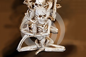 Skeletons in a row doing yoga with one foot up under their arms sitting in a orangish brown blurred background
