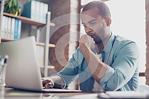 Skeptic young afro freelancer is making decision sitting at the office in casual smart, analyzing the data in the computer photo