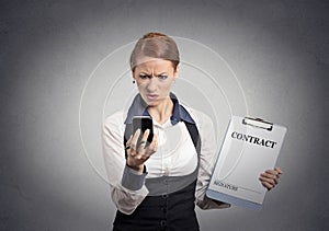 Skeptical businesswoman holding contract looking on smartphone