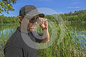 Skeptical look. Man in cap watches from under sunglasses with contempt, doubtful and scepticism outdoors