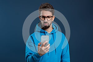 Skeptical man wearing glasses looking at smartphone screen