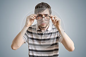 Skeptical or suspicious man is looking at you and touching glasses