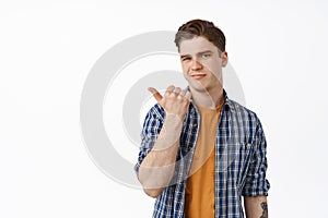 Skeptical and unamused young man pointing left, showing something lame or uninteresting, complaining, express doubt and