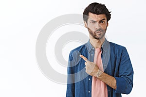 Skeptical, uncertain and suspicious handsome 25s man with beard, frowning smirk unsure, pointing left and staring