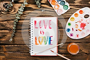 sketchbook with handlettering inscription `Love is love` on wooden table