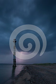 Skew lighthouse in the Baltic Sea. Stormy night and lightning.