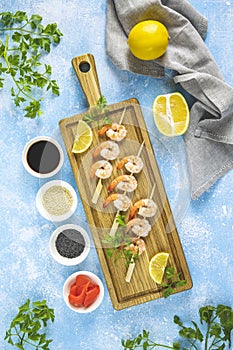 Skewers shrimp barbecue served on wood cutting board with lemon or lime in top view. Delicious grilled prawn with spices for