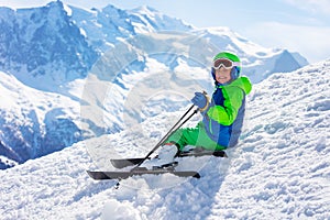 Ski boy sit on snow with mountain peak background