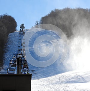 Ski chairlift climbing ski slope with snow making machine clouds of snow