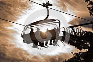 Four skiers on a chair lift against the backdrop of the sun, contour photo, orange shades, ski region Schladming Dachstein Austria