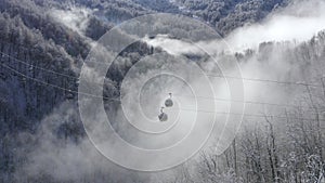 Ski elevator moving over white snowy mountain cloud forest in lowland. Drone view ski lift transporting skiers and snowboarders to