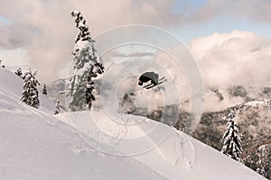 Ski freerider jumping from snow-capped mountain slope on background of trees and cloudy sky