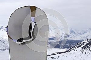 Ski goggles dangling on a standing snowboard stuck in the snow