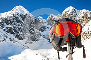Lyžiarska prilba googles na lyžiarskej palici so zasneženými vrcholmi na pozadí