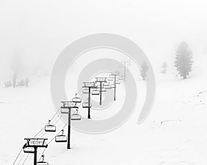 Ski lift disappearing into the fog on a snow covered mountain.