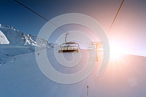 Ski lift empty ropeway on hilghland alpine mountain winter resort on bright sunny evening . Ski chairlift cable way with people