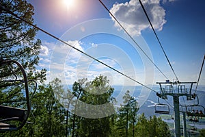 Ski lift in the mountains on sunny day against blue sky, white clouds, green hills and mountain lake. Mountain valley with cable