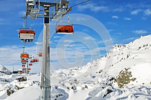 Ski lift ropeway on hilghland alpine mountain winter resort on bright sunny day. Ski chairlift cable way with people enjoy skiing