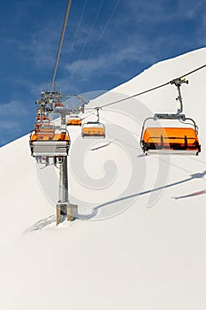 Ski lift ropeway on hilghland alpine mountain winter resort on bright sunny day. Ski chairlift cable way with people