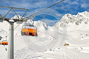 Ski lift ropeway on hilghland alpine mountain winter resort on bright sunny day. Ski chairlift cable way with people