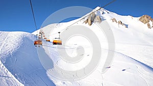 Ski lift ropeway on hilghland alpine mountain winter resort on bright sunny day. Ski chairlift cable way with people