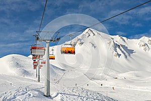 Ski lift ropeway on hilghland alpine mountain winter resort on bright sunny day. Ski chairlift cable way with people enjoy skiing