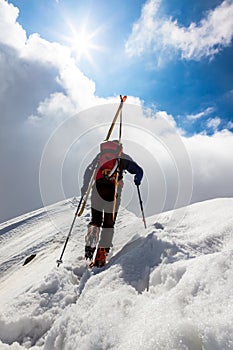 Ski mountaineer walking up along a steep snowy ridge with the s