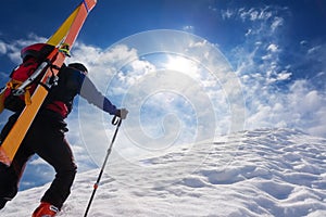 Ski mountaineer walking up along a steep snowy ridge with the s