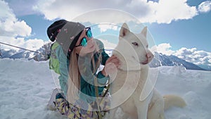 Ski resort entertainments. Friends have fun on the ski resort. Young girl with blonde hair caress siberian husky