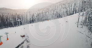 Ski resort with people at pine forest aerial. Tourists snowboarding down hill at sunrise. White snow