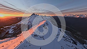 Ski resort on snow mountain ridge summit surrounded by pink golden sunset